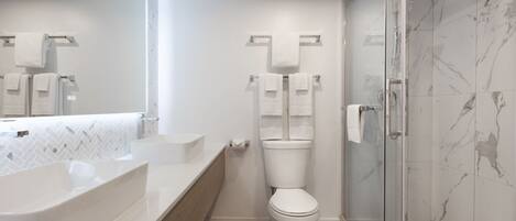 A modern bathroom with a large white sink, a toilet, and a glass shower enclosure.