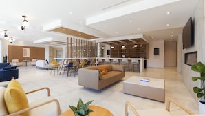 Un hall d’hôtel moderne doté d’un espace salon central, d’un bar et d’un espace repas.