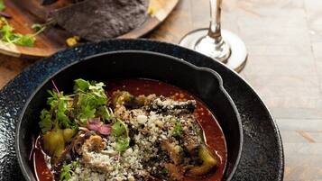 Un plato en sartén con comida, un vaso de bebida y una tabla de madera con alimentos.
