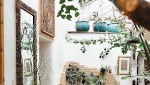 A cozy living room with a sofa, a coffee table, and a fireplace. There are potted plants and a wall with decorative elements.