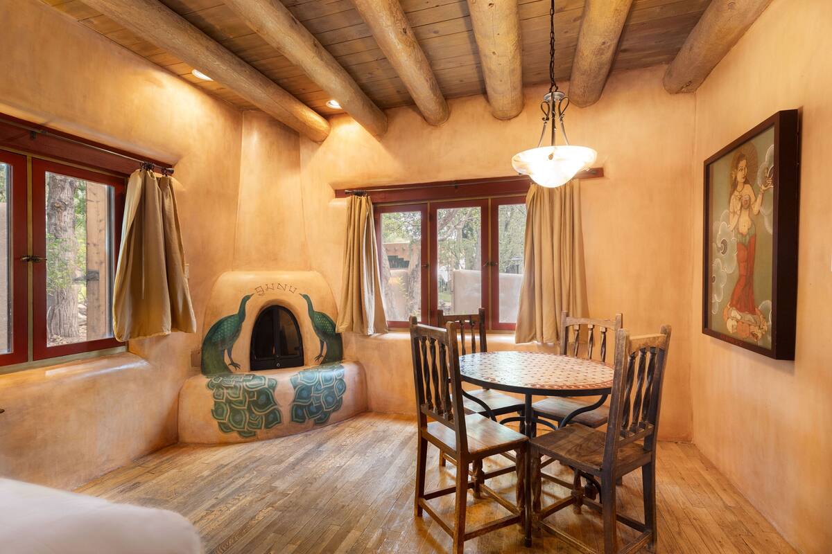 A cozy dining area with a round table and wooden chairs, a fireplace with a peacock design, and a painting on the wall.