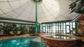 An indoor swimming pool with a stone surround, lounge chairs, and a large glass window.