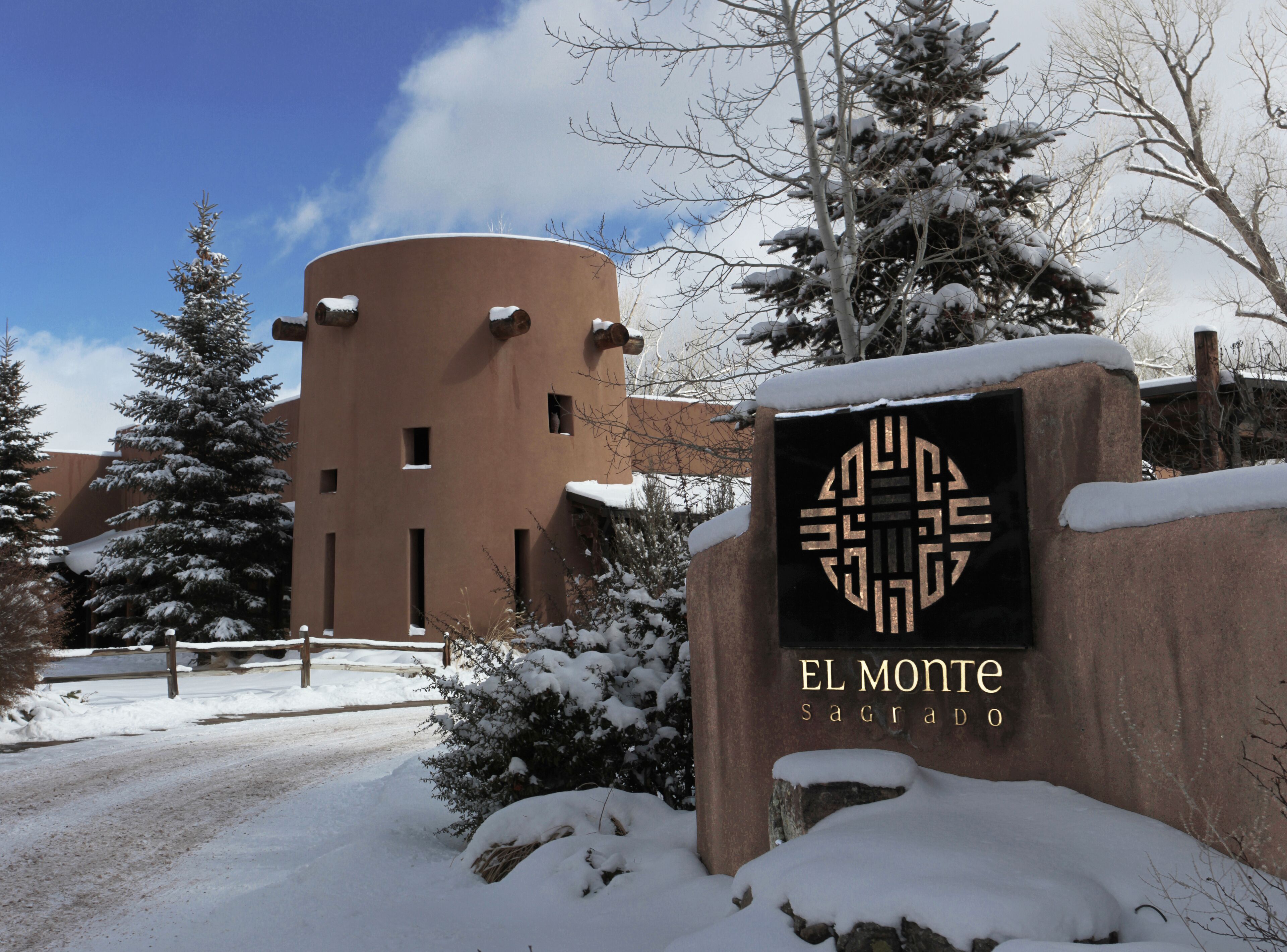 A snow-covered sign with "EL MONTE SAGRADO" and a building in the background.
