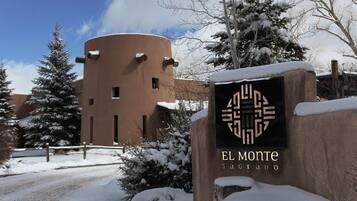 Um sinal coberto de neve com a inscrição 'EL MONTE SAGRADO' e um edifício ao fundo.