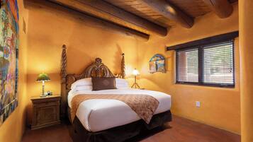 A bedroom with a wooden bed, a nightstand with a lamp, a wall-mounted clock, and a window with blinds.