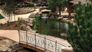 A bridge over a stream with a waterfall, surrounded by trees and a small pond.