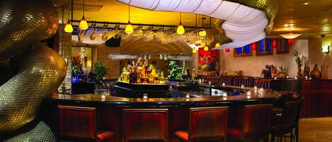 Zona de bar con barra circular, varios taburetes, luces colgantes y una gran pieza decorativa con forma de serpiente.