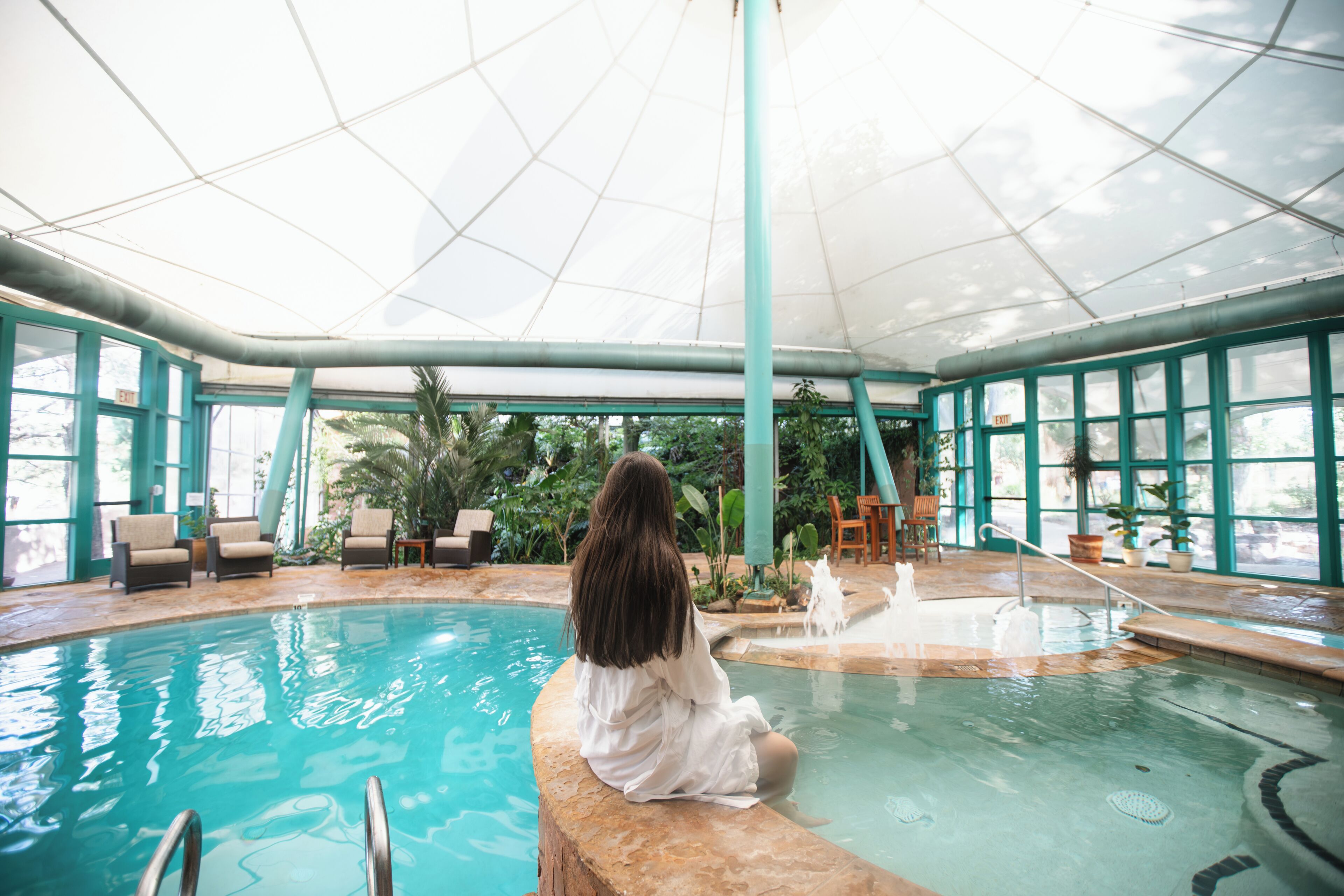A pool area with a glass ceiling, indoor seating, and a fountain.