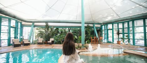 A pool area with a glass ceiling, indoor seating, and a fountain.