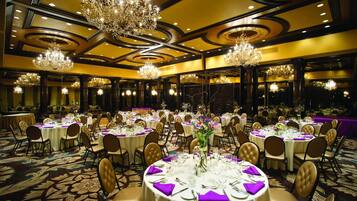 A banquet hall with round tables, chairs, and chandeliers.