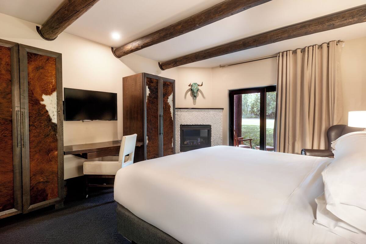 A hotel room with a large bed, a flat-screen TV, a wooden wardrobe, and a fireplace.