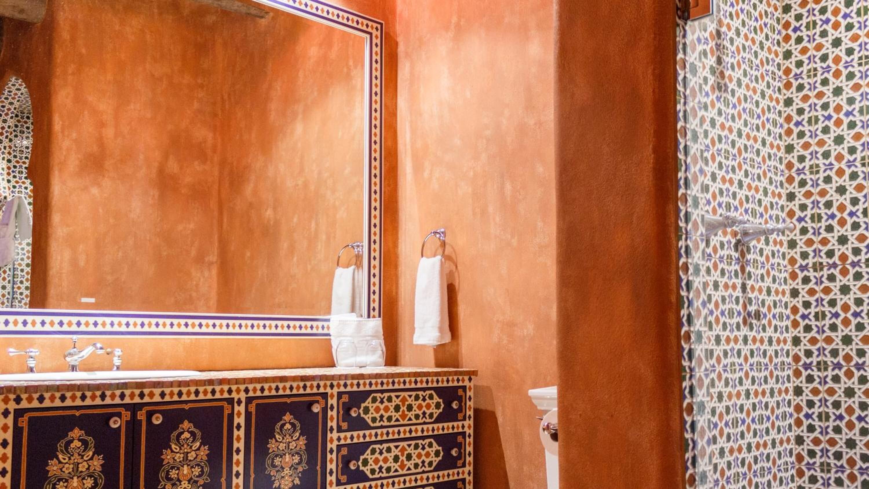 A bathroom with a large mirror, a sink with a decorative cabinet, and a shower area with patterned tiles.