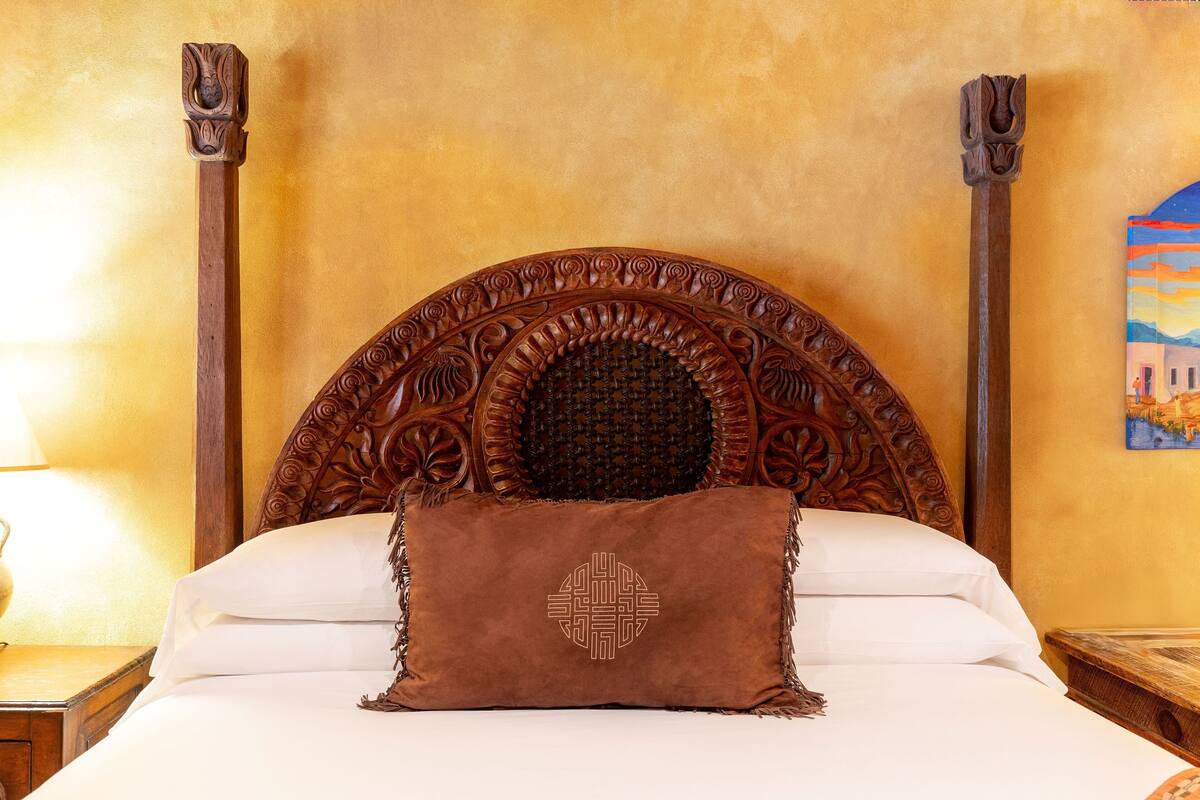 A bed with a wooden headboard, a brown pillow, and a painting on the wall.