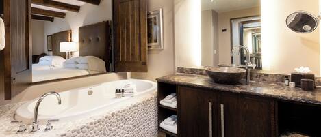 A modern bathroom with a stone-textured bathtub, a large mirror, and wooden cabinetry.