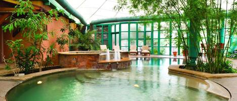 Une piscine intérieure agrémentée d’une cascade, entourée d’espaces de détente et d’une végétation luxuriante.