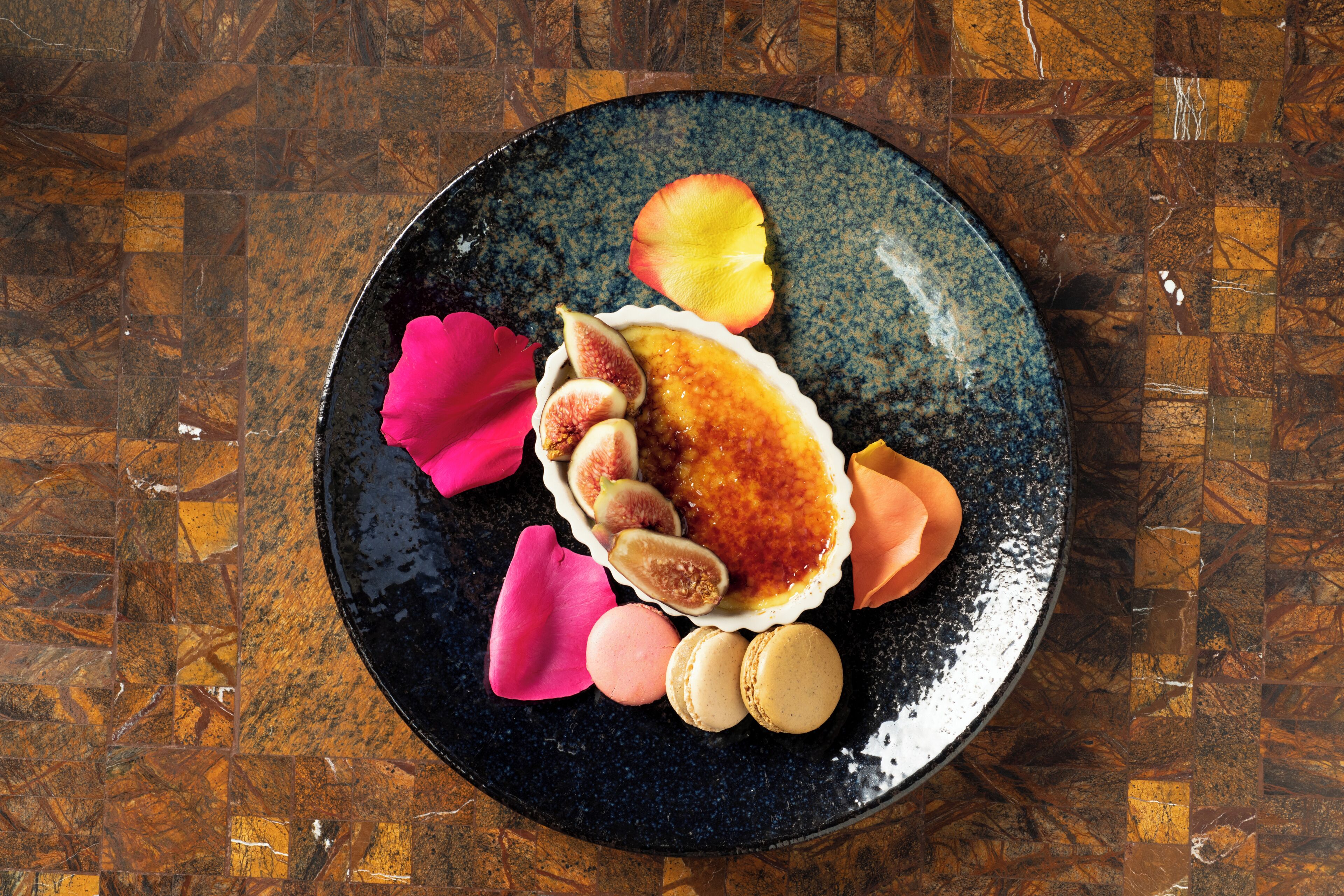 A plate with a dessert, including a custard, figs, and macarons, on a dark ceramic plate.