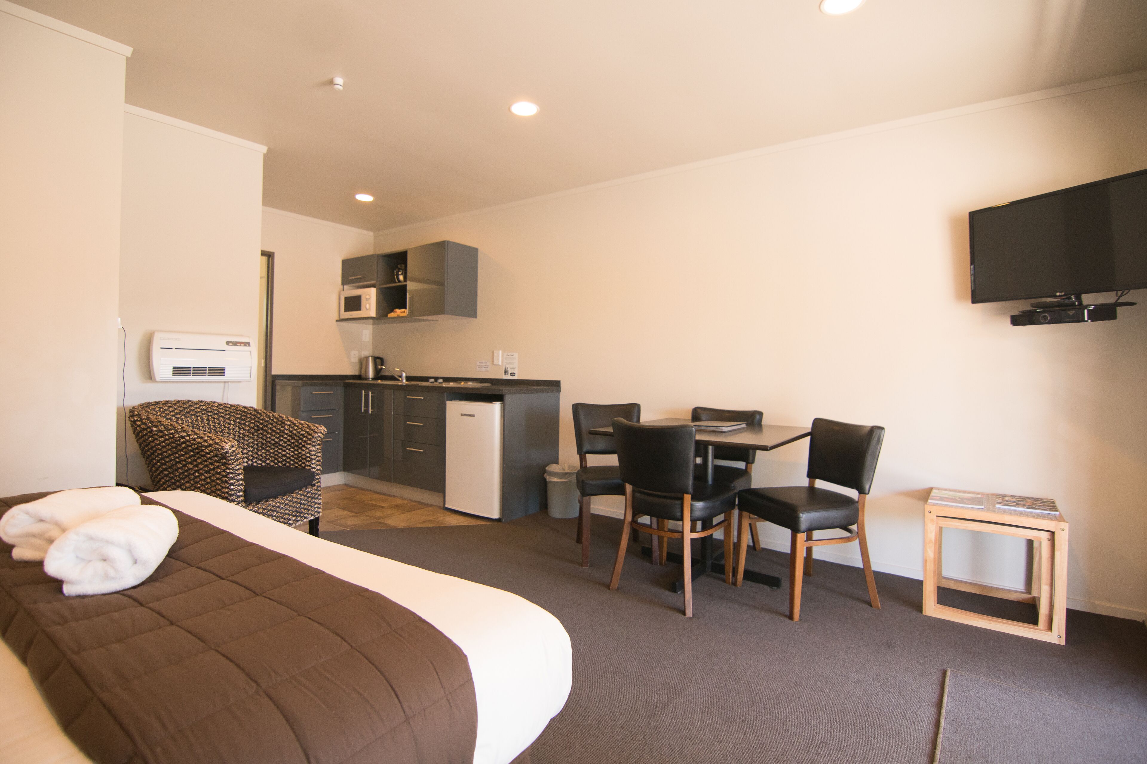 A hotel room with a bed, a desk, a chair, a television, a microwave, and a small kitchenette.
