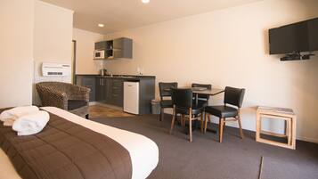A hotel room with a bed, a desk, a chair, a television, a microwave, and a small kitchenette.