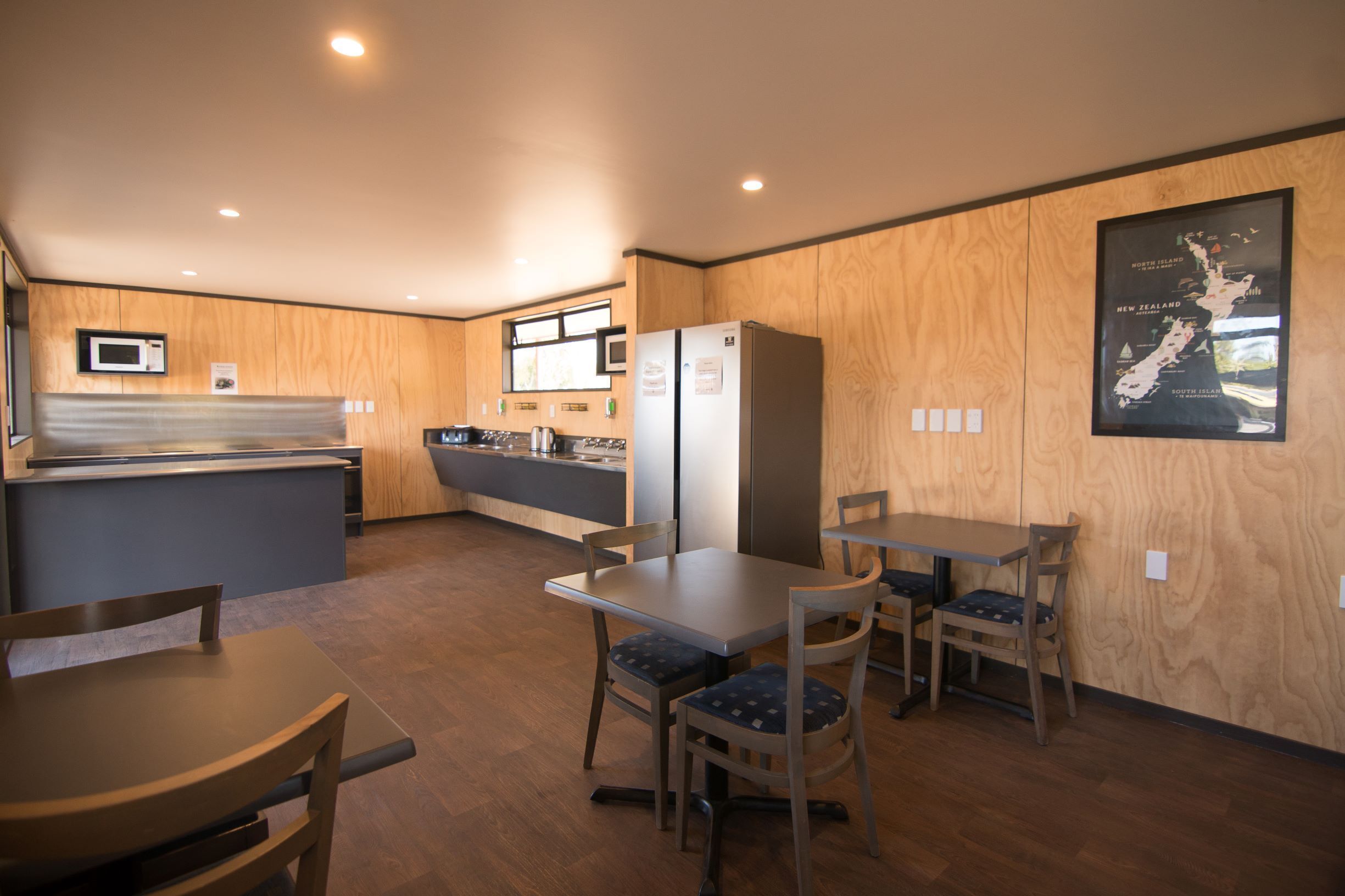 A modern kitchen with wooden cabinetry, a refrigerator, a microwave, and a dining area with a table and chairs.