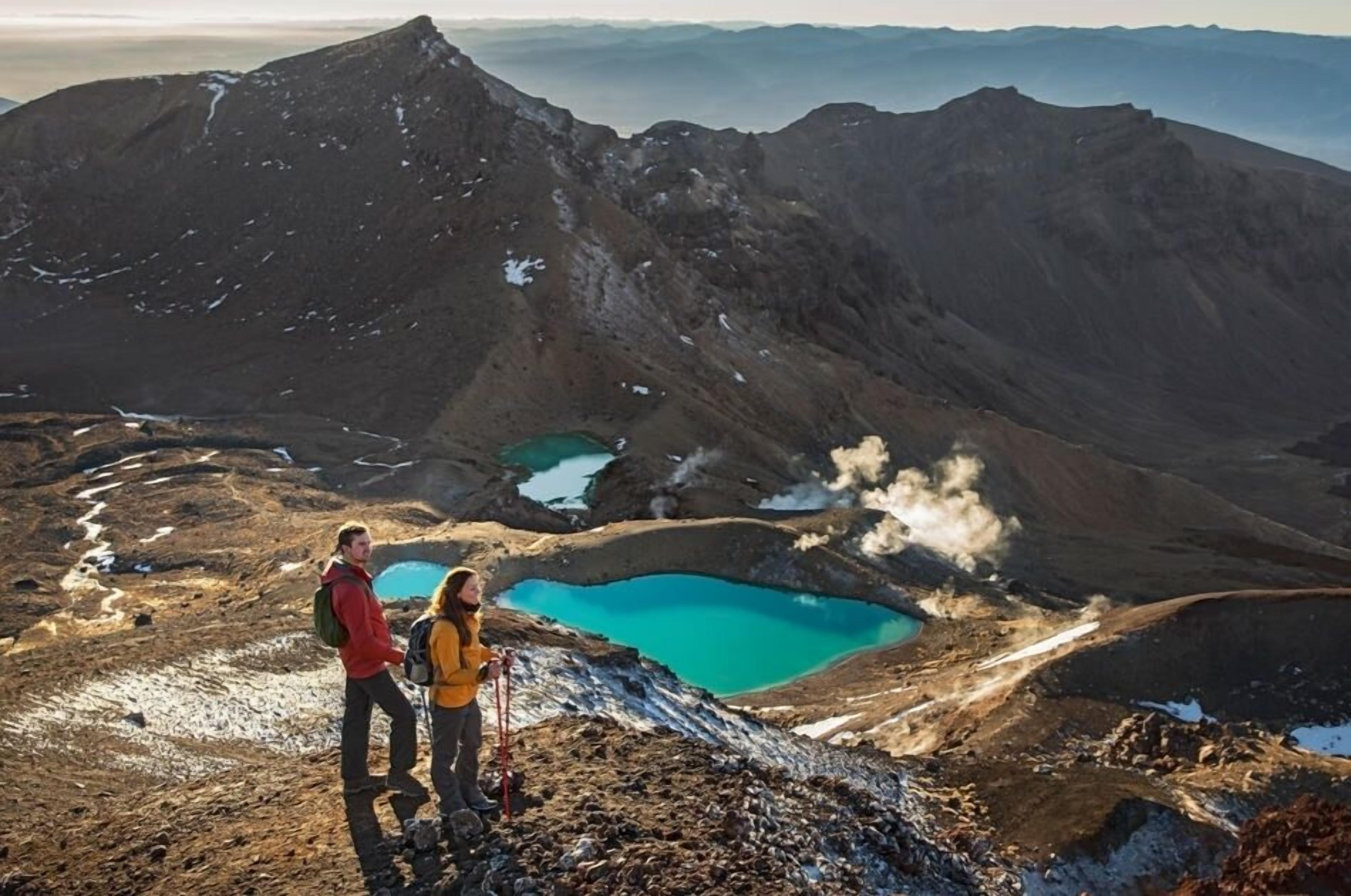 A mountainous landscape with two turquoise lakes and a person standing on a rocky outcrop.