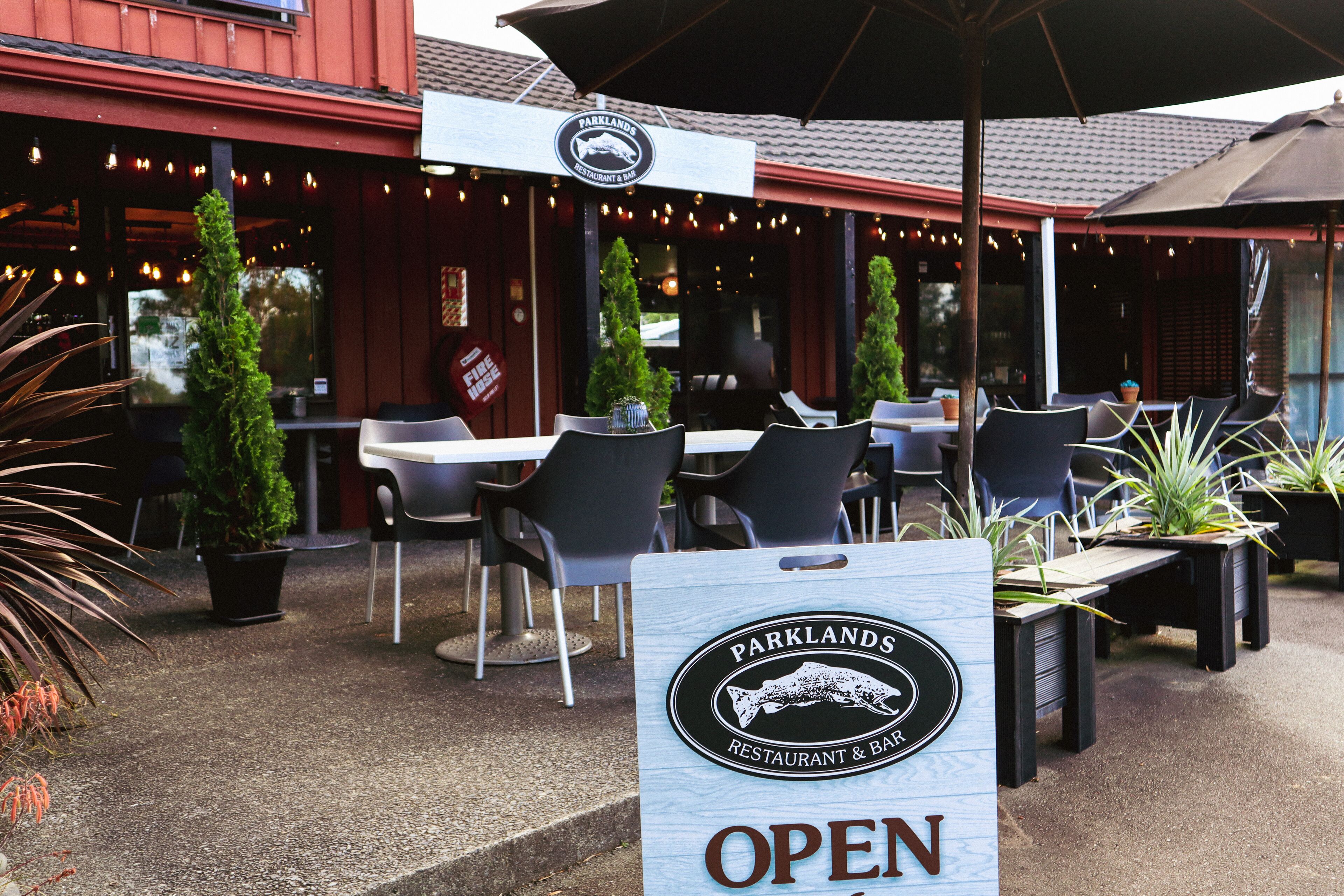 An outdoor seating area with tables and chairs, a sign indicating the restaurant is open, and a signboard with the restaurant's name.