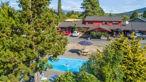 A resort with a swimming pool, red buildings, and surrounding greenery. - Parklands Motorlodge (Turangi)