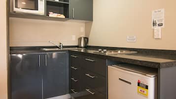 Una cocina compacta con armarios oscuros, un microondas, un lavamanos y un refrigerador.