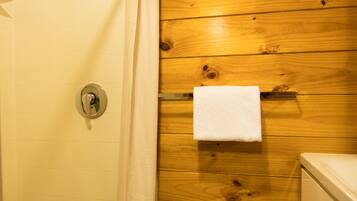A shower with a curtain, a towel hanging on the wall, and wooden paneling.