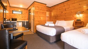 A wooden cabin-style room with a bed, two bedside tables, a desk, and a chair. - Parklands Motorlodge (Turangi)