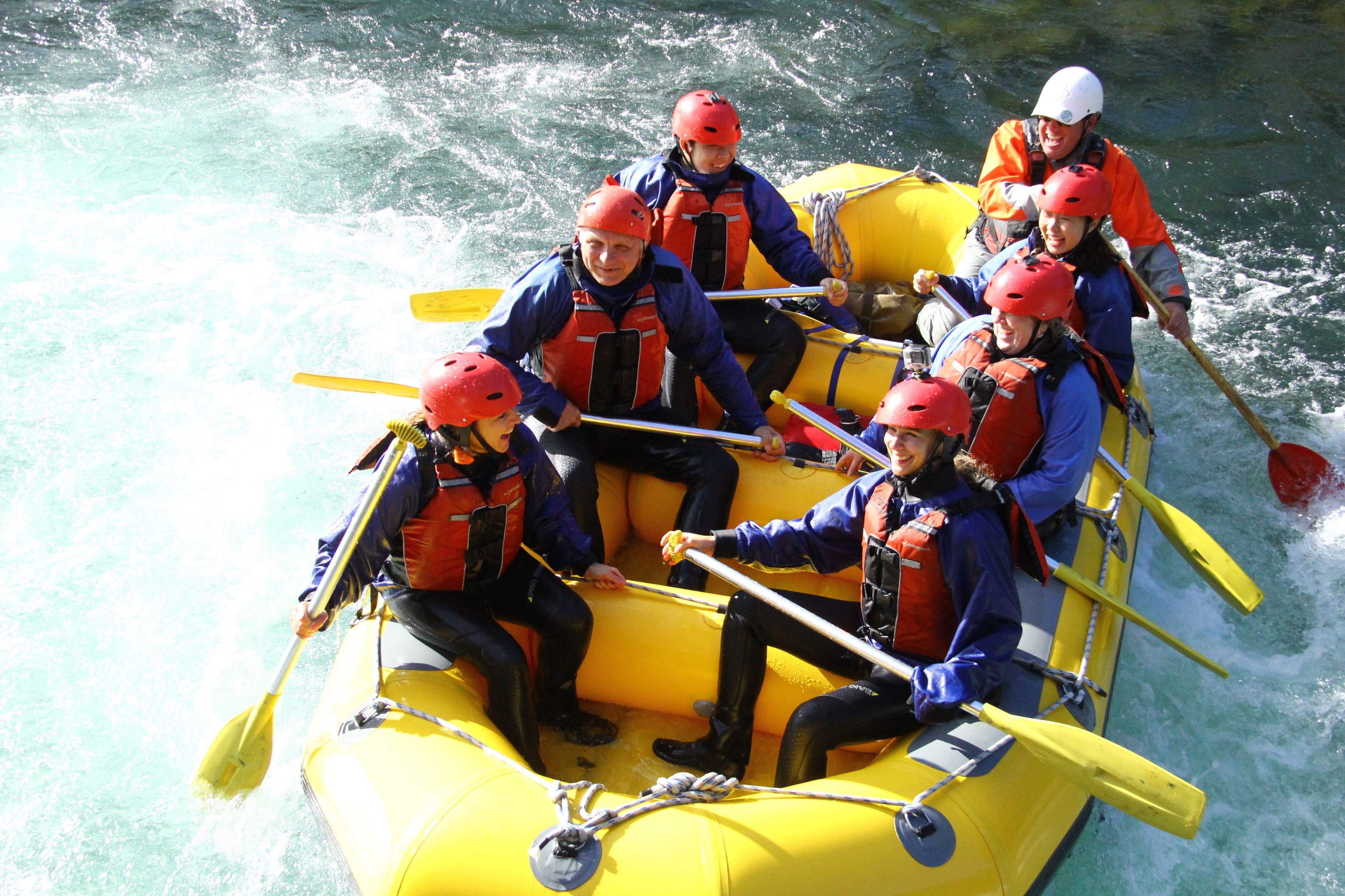 A group of people in a yellow raft with paddles, wearing life jackets and helmets, on a body of water.