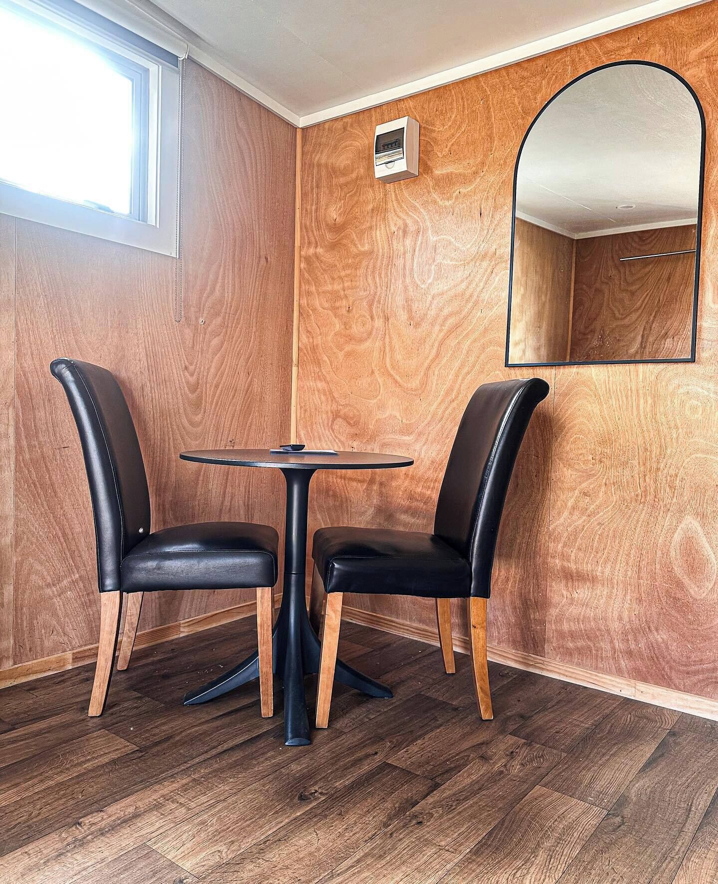 A room with two black leather chairs and a small round table, wooden panel walls, a small mirror, and a window.