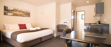 Quarto de hotel com cama, mesa de jantar e cozinha compacta.