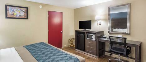 A hotel room with a bed, a desk with a computer, a television, and a red door.