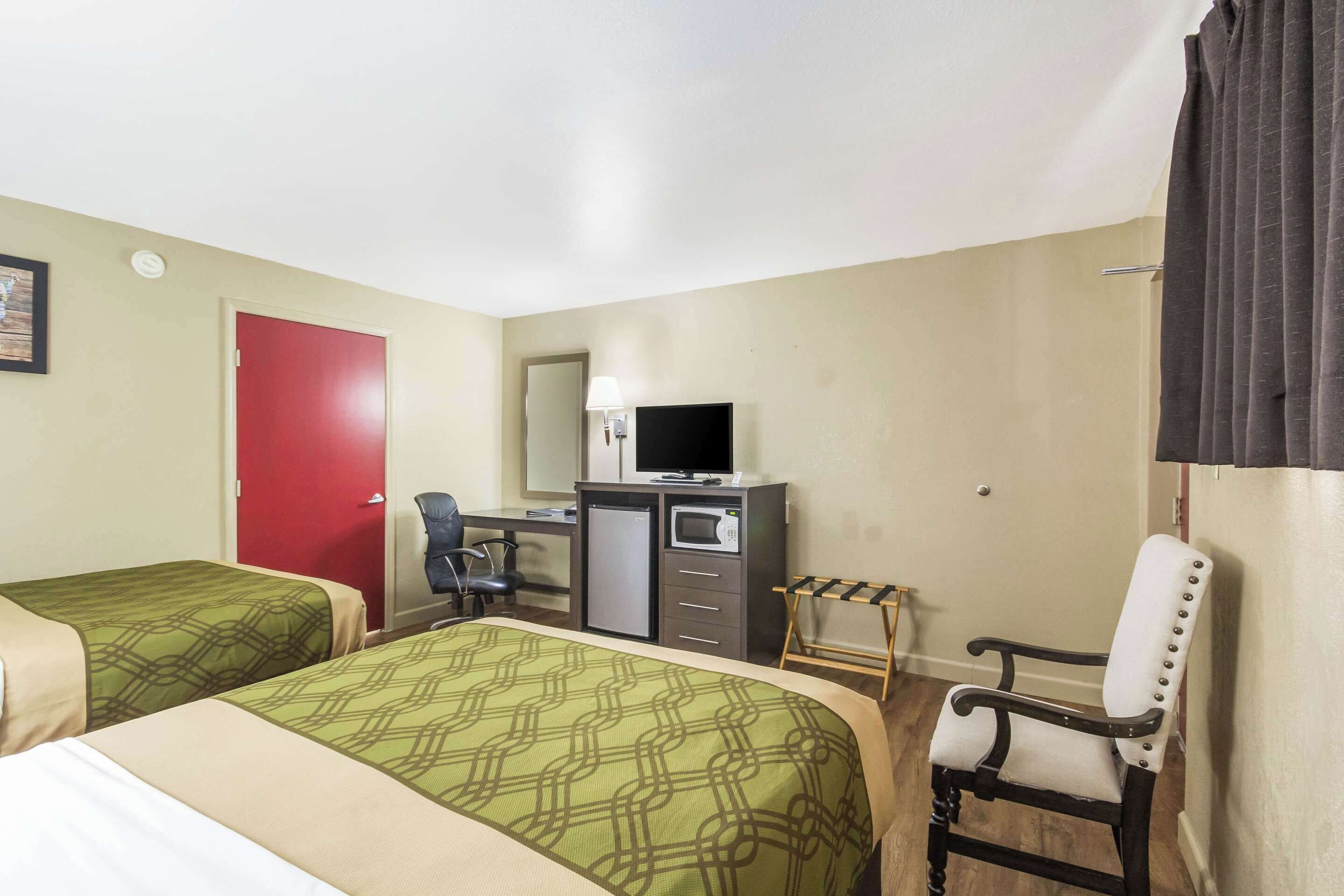 A hotel room with two beds, a desk with a computer and a TV, a chair, and a small table.
