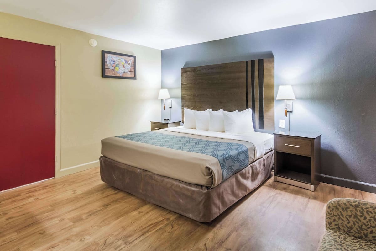 A hotel room with a large bed, two bedside tables with lamps, a red door, and a framed picture on the wall.