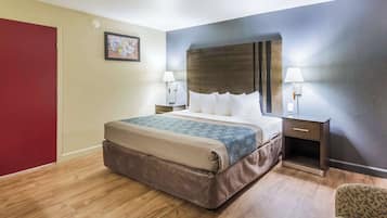 Una camera d'albergo con un letto grande, due comodini con lampade, una porta rossa e un quadro appeso al muro.