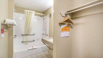 A bathroom with a bathtub, a shower, and a sink. There are towels on a shelf and a hanging rack.