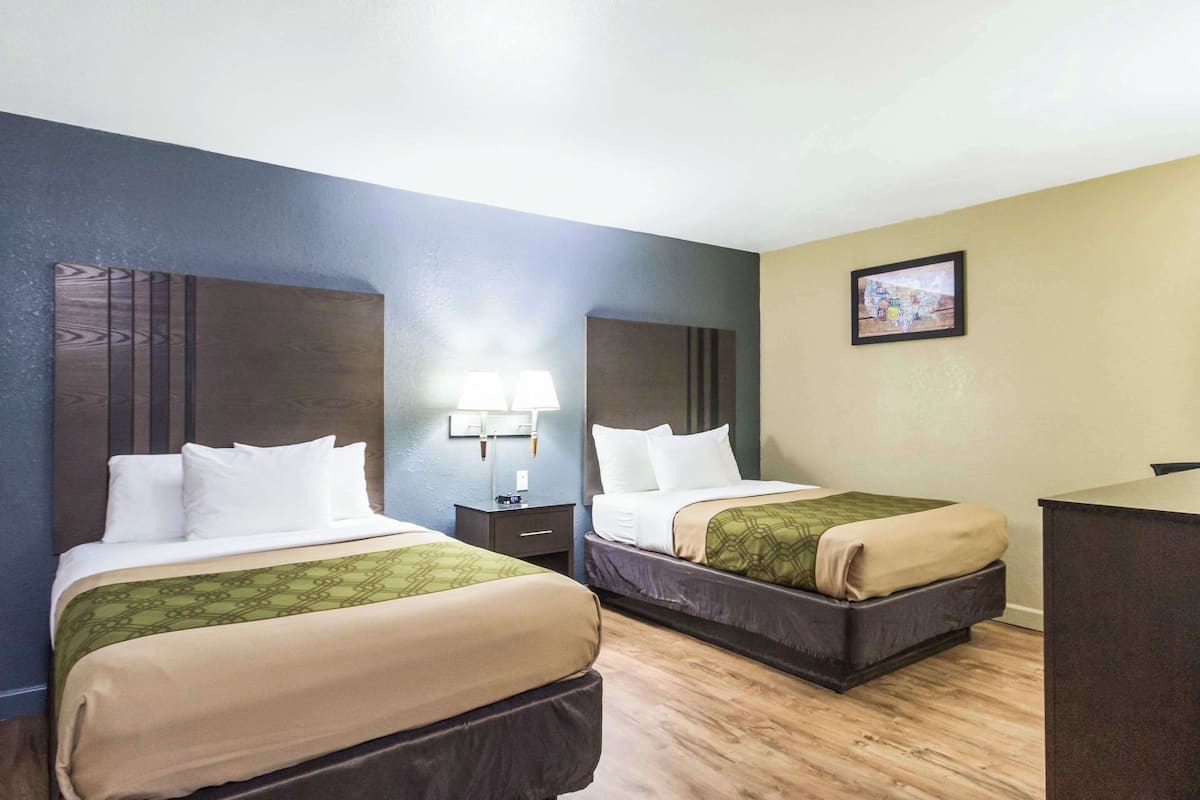 A hotel room with two beds, a desk, a lamp, and a picture on the wall.