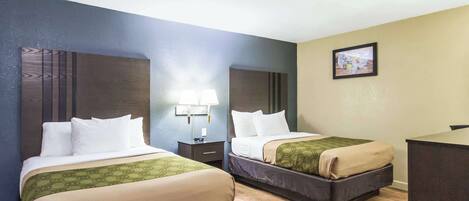A hotel room with two beds, a desk, a lamp, and a picture on the wall.