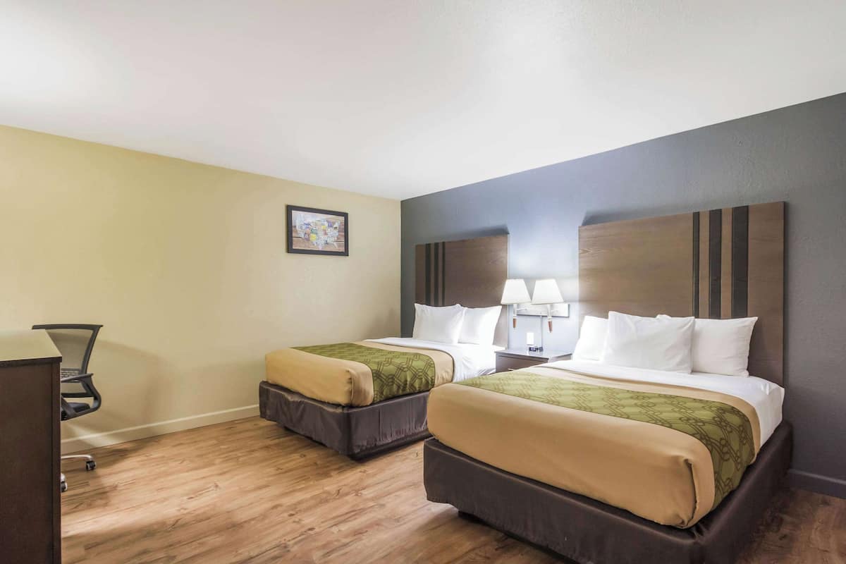 A hotel room with two beds, a desk, and a chair.