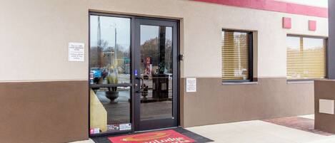 A hotel entrance with a glass door, a non-smoking sign, and a mat with the hotel name.