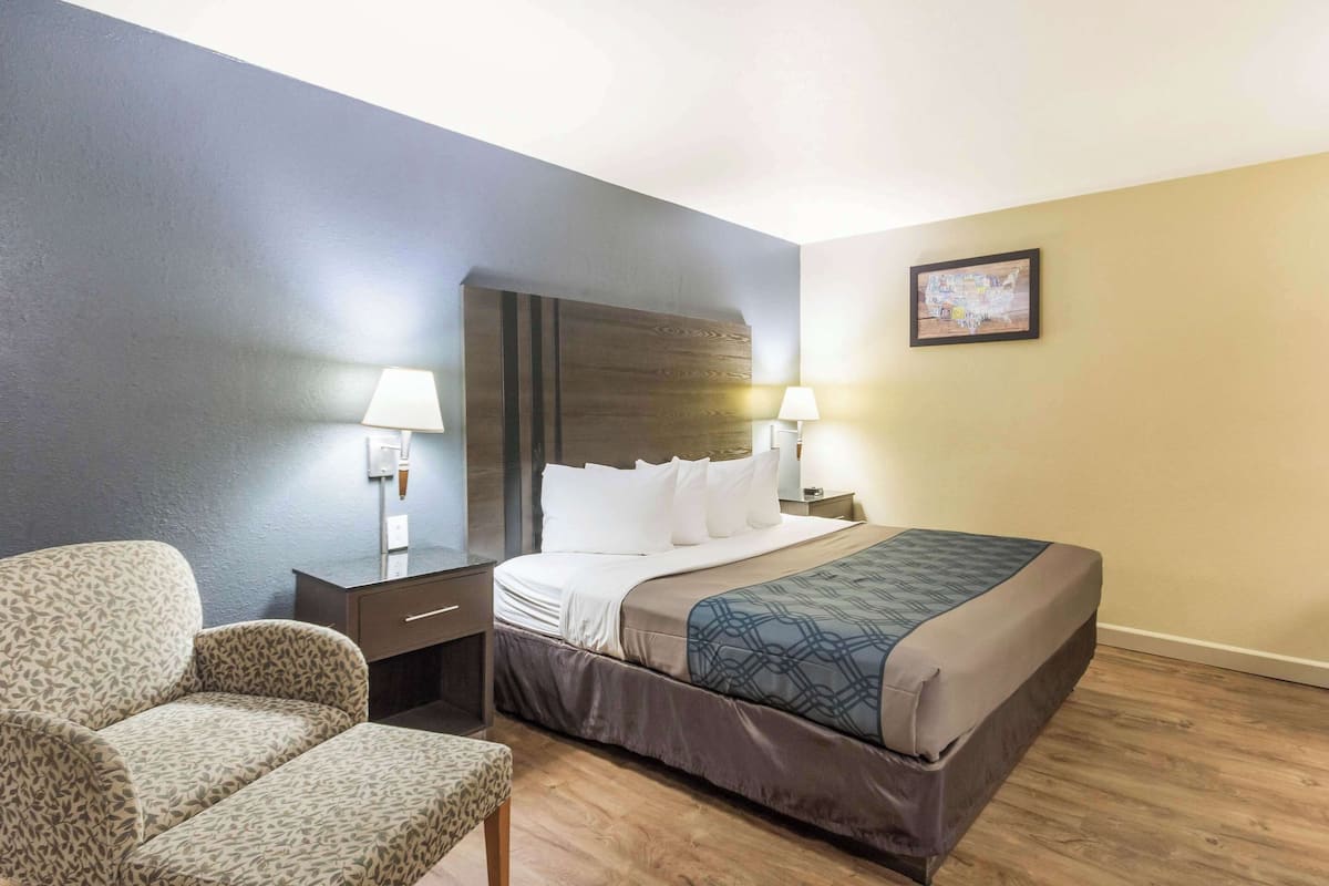 A hotel room with a bed, a chair, a nightstand, and two wall lamps.