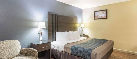 A hotel room with a bed, a chair, a nightstand, and two wall lamps.