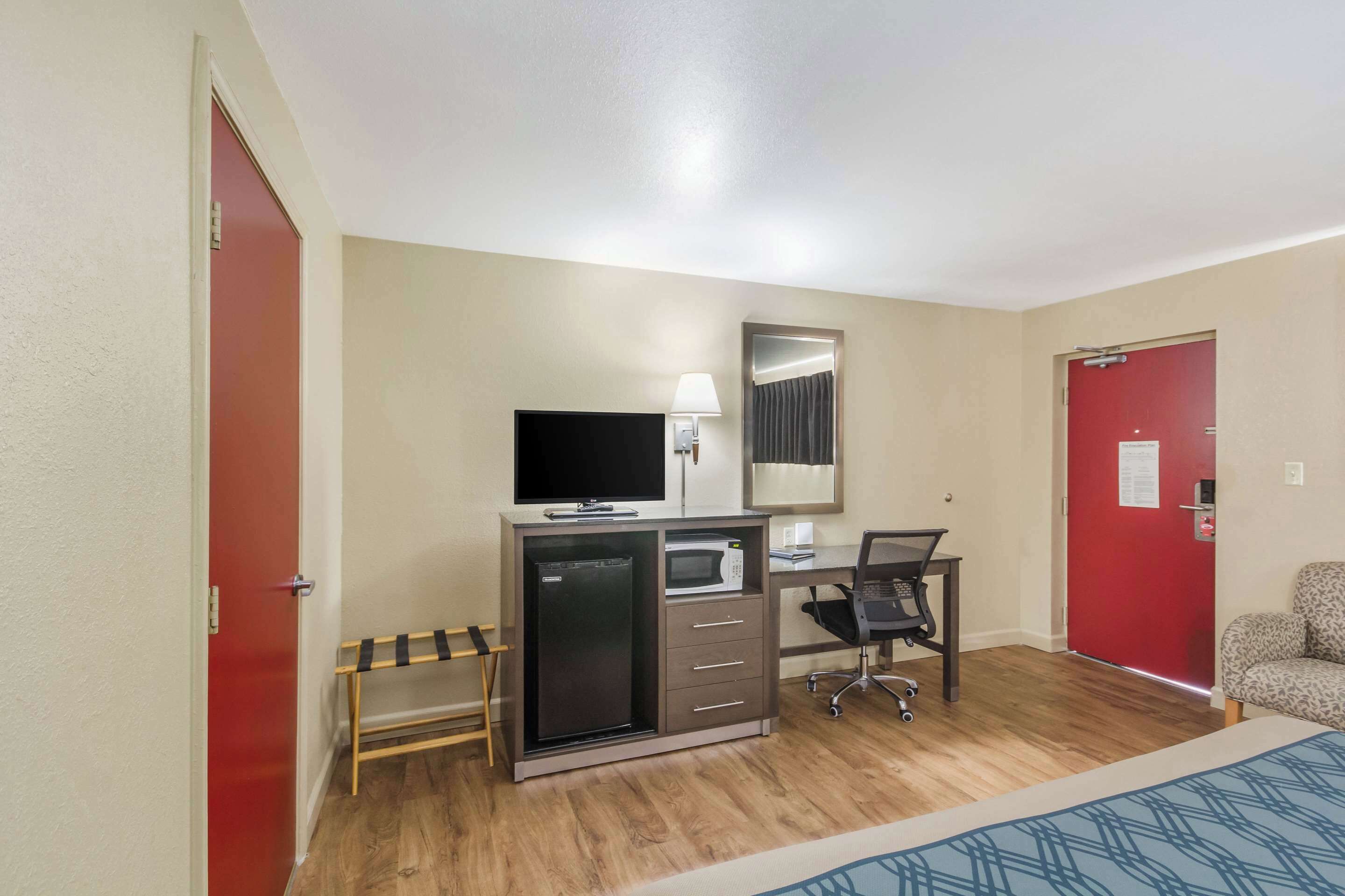 A hotel room with a bed, a desk with a computer, a TV, a microwave, and a refrigerator.