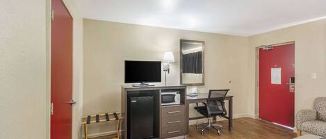 A hotel room with a bed, a desk with a computer, a TV, a microwave, and a refrigerator.