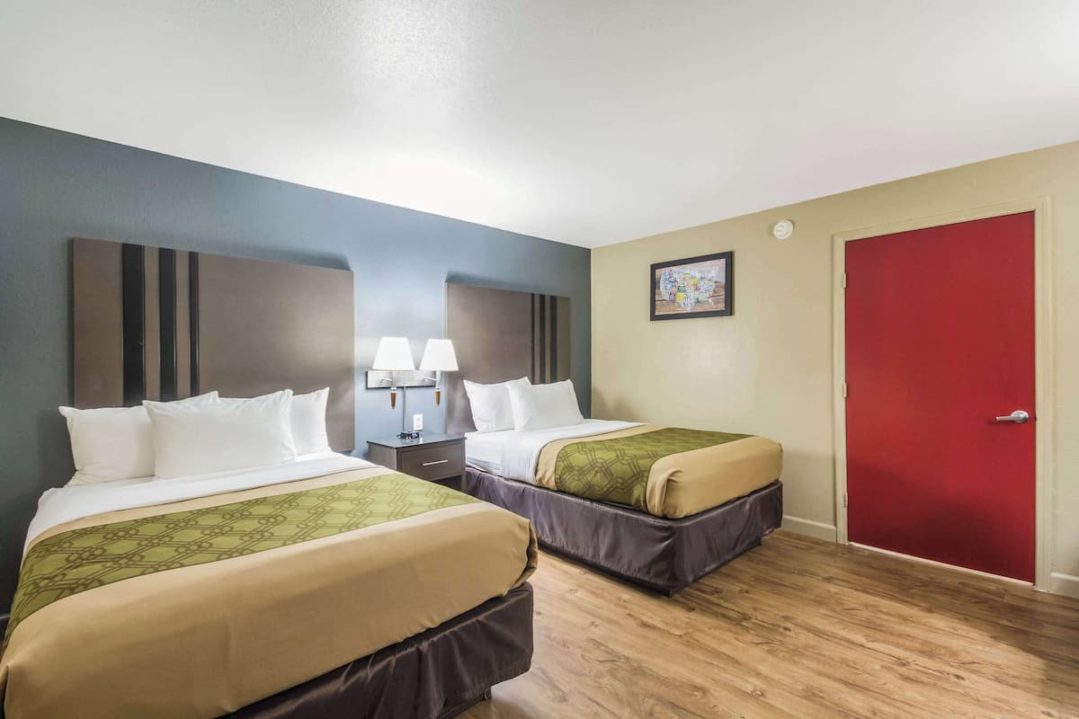 A hotel room with two beds, a red door, and a nightstand with lamps.