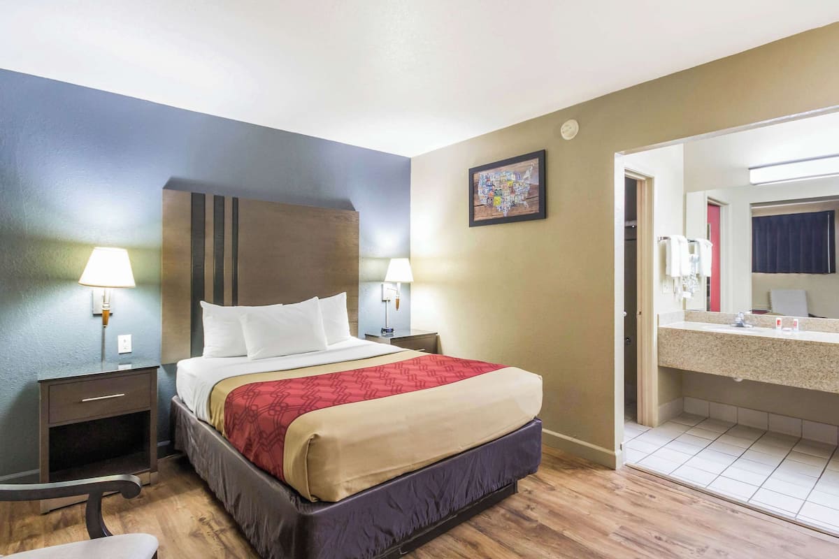 A hotel room with a bed, bedside lamps, a nightstand, a chair, a bathroom with a sink and mirror.