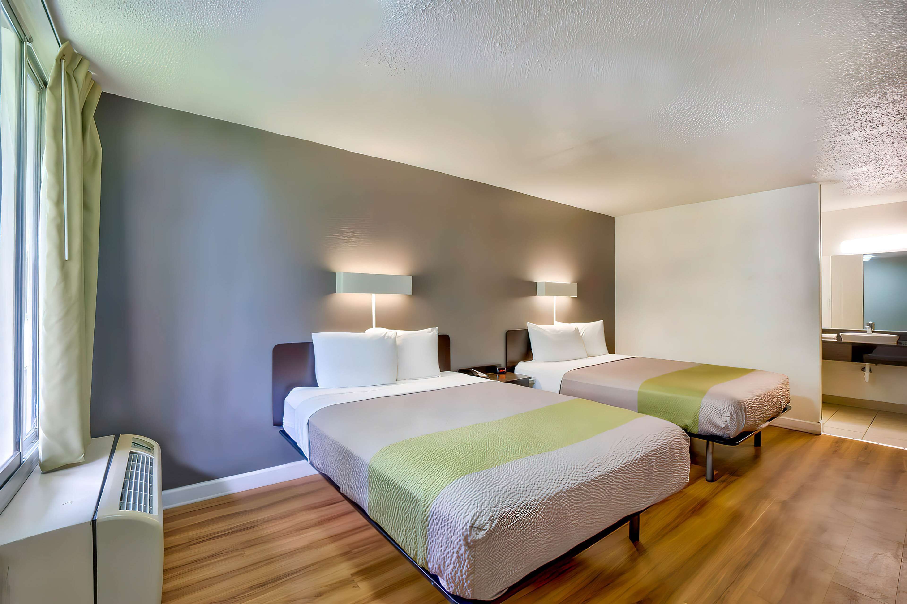 A hotel room with two beds, a window with curtains, a heater, and a mirror.