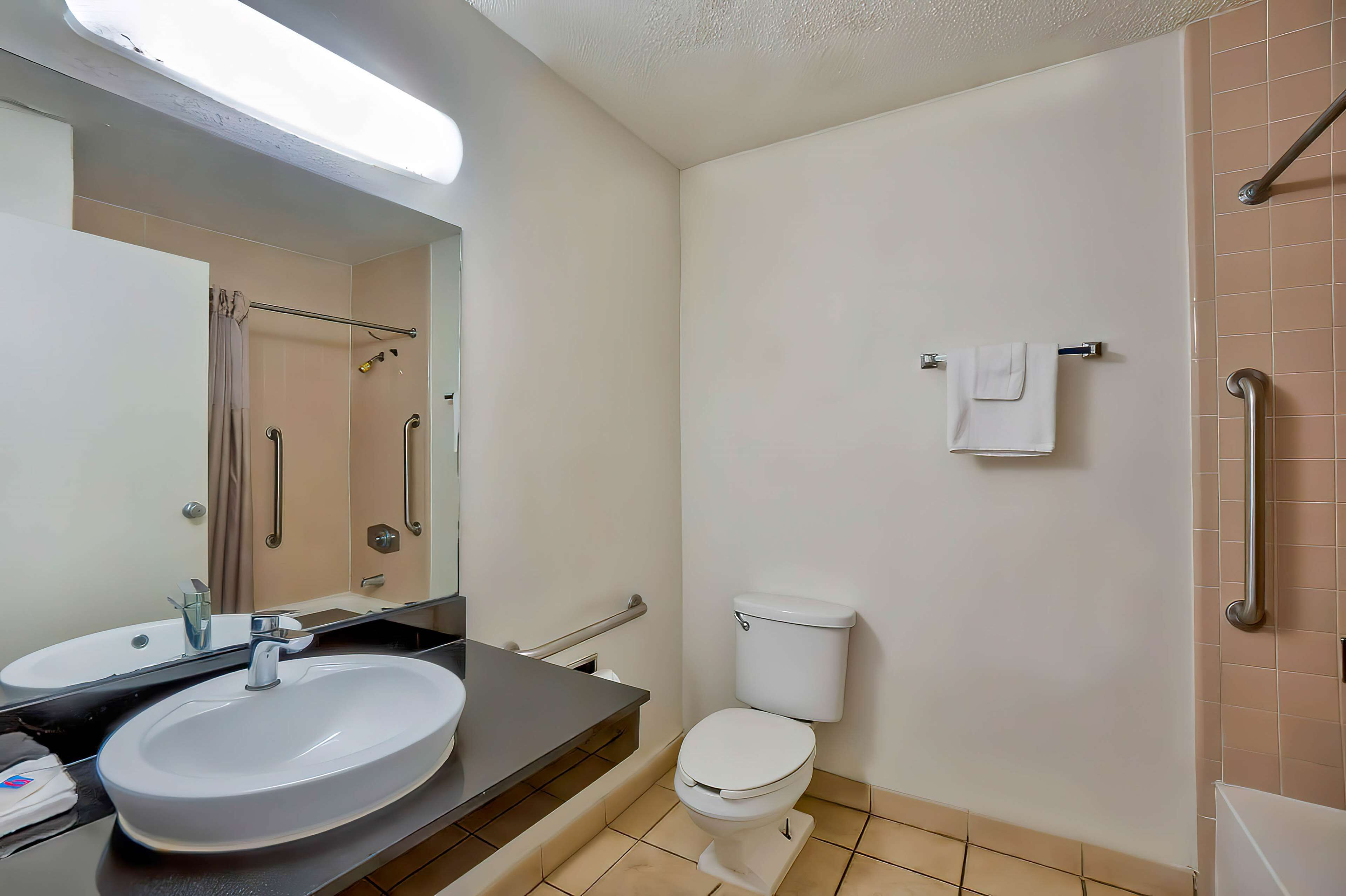 A bathroom with a sink, toilet, and handrails.