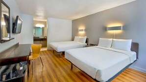 A hotel room with two beds, a desk, a chair, and a television.